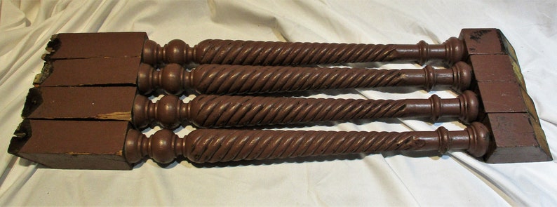 May include: Four dark brown wooden table legs with a twisted design. Each leg has a rounded top and a square base.