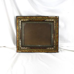 May include: A rectangular picture frame with a dark brown and gold patterned border. The frame has a dark interior and a decorative design with white accents. The frame is sitting on a white surface.