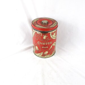 May include: A vintage red coffee tin with a gold floral design and the word "Coffee" in a decorative script. The tin has a lid with a small knob and the word "Hellick" is printed below "Coffee".