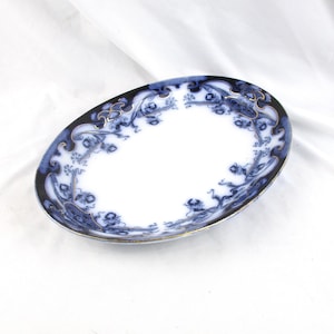 May include: Oval-shaped, white ceramic dish with a blue floral pattern and gold trim. The dish has a dark blue border with ornate designs. A classic piece for serving or display.