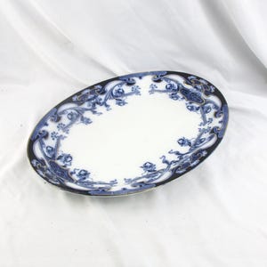 May include: Oval porcelain serving dish with a white center and a dark blue and black border. The border features a detailed floral and scroll design in blue. The dish is set against a white background.