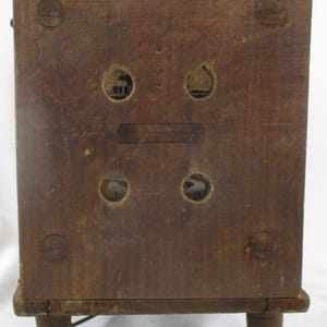May include: A vintage wooden radio cabinet with a dark brown finish. The back of the cabinet features four circular openings, two rectangular openings, and four small wooden feet. The cabinet has a rectangular shape.