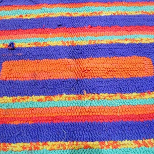 May include: A colorful rug with a rectangular design. The rug is made of looped fabric and has stripes of orange, red, blue, yellow, and green.