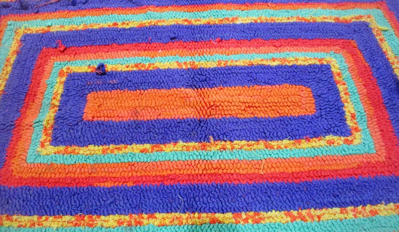 May include: A colorful rug with a rectangular design. The rug is made of looped fabric and has stripes of orange, red, blue, yellow, and green.