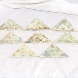 May include: Nine triangular tiles with a marbled appearance, featuring shades of cream, brown, and blue-green. The tiles are arranged in a triangular pattern on a white fabric background. The tiles appear to be ceramic or stone.