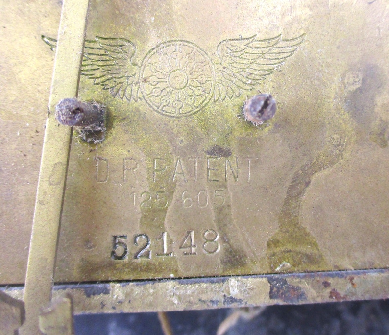 Peut inclure: Gros plan d'une plaque en laiton avec le texte "D.P. PATENT" et les chiffres "125 605" et "52148". La plaque pr&eacute;sente un embl&egrave;me d&eacute;coratif avec des ailes et un motif circulaire. Le laiton a un aspect terni.
