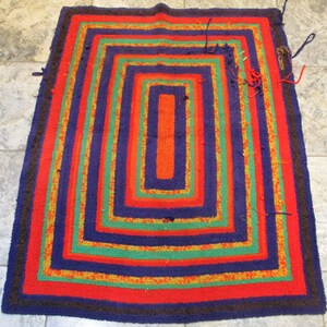 May include: A colorful braided rug with a multi-layered design. The rug features stripes of red, orange, yellow, green, and blue.