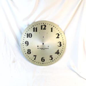 May include: A vintage clock face with black numerals on a silver-colored background. The numbers 1 through 12 are evenly spaced around the circular face. The text "SELF WINDING CLOCK CO. NEW YORK" is printed at the bottom.