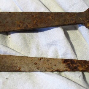 May include: Two rusty metal hinges with rounded ends and a hole in the center. The hinges are on a white fabric background.