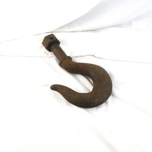 May include: A large, rusty metal hook with a threaded bolt and hexagonal nut. The hook curves downward, and the metal has a weathered, aged appearance. The item is likely used for heavy-duty lifting or securing.