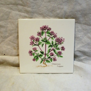 May include: A white ceramic tile with a botanical illustration of oregano, featuring pink flowers and green leaves. The text "Origanum Vulgare" is printed below the plant.