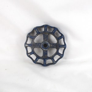May include: A vintage, circular valve handle with a dark blue, weathered finish. The handle features a series of open, rounded sections radiating from a central hub. The metal shows signs of age and use.