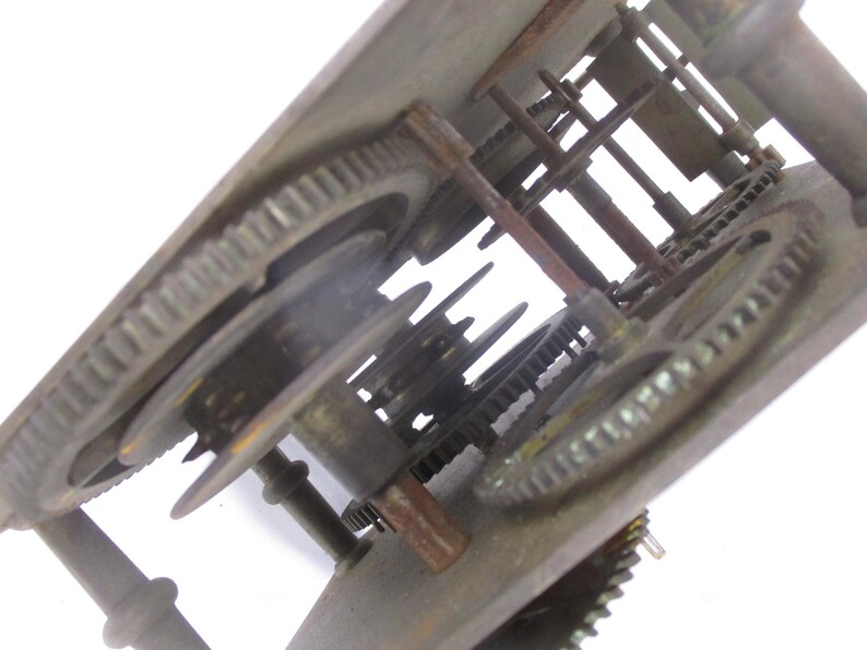May include: Close-up of a vintage clock mechanism. The image shows a complex arrangement of metal gears, rods, and other components. The gears are various sizes and have a worn, aged appearance, suggesting the clock's age. The overall color is a mix of bronze and rust.