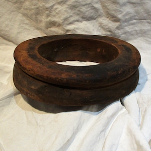 May include: A dark brown wooden ring with a smooth, worn surface. The ring is made of two pieces of wood that are stacked on top of each other.