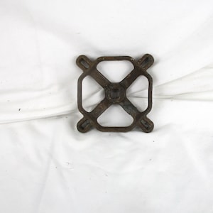 May include: A rusty metal square-shaped base with four holes and a cross-shaped design in the center.