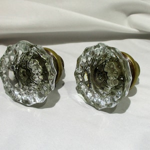 May include: Pair of antique glass door knobs with brass bases. The glass is clear and has a faceted design.