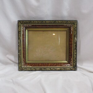 May include: A rectangular picture frame with a brown, gold, and green wood finish. The frame has a decorative inlay of white wood.