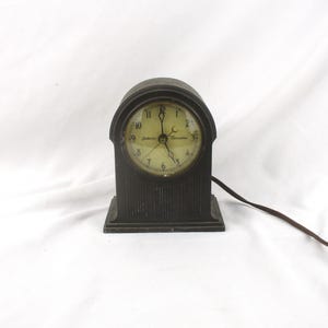 May include: A black vintage electric clock with a white face and black hands. The clock has a rectangular base and a rounded top. The clock face has the text "South Bend Electric" printed on it.