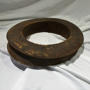 May include: A large, dark brown wooden ring with a wide, flat surface and a smaller, raised inner ring. The ring is made of rough-hewn wood and has a rustic appearance.
