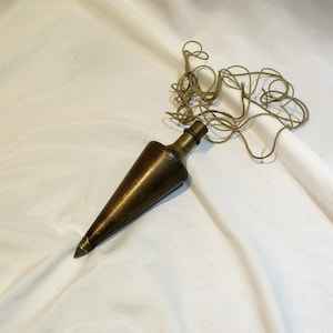 May include: A brass plumb bob with a pointed tip and a string attached. The string is coiled and tangled.