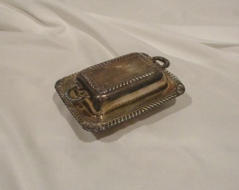 May include: Silver butter dish with a lid and two handles. The dish has a decorative rope-like border.