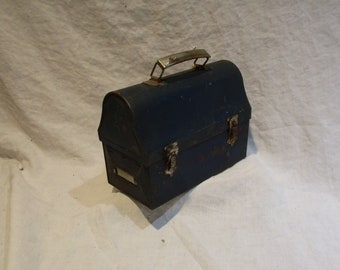 May include: A vintage blue metal lunchbox with a silver handle and two clasps. The lunchbox has a label on the front.