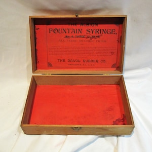 May include: A wooden box with a red interior and a label that reads "The Albion Fountain Syringe, No. 4 Three Quarts, All Hard Rubber Pipes, The Davol Rubber Co., Providence, R.I. U.S.A."