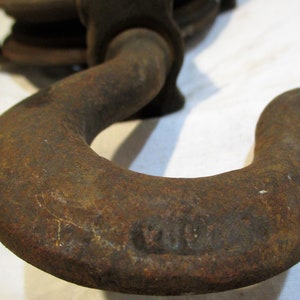 May include: Close-up of a rusty metal hook with a rounded shape. The hook is part of a vintage chain hoist.
