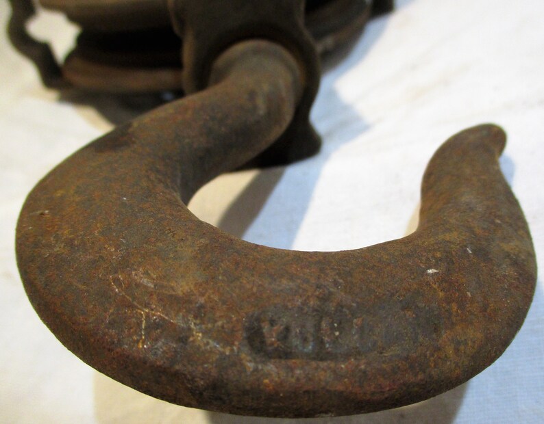 May include: Close-up of a rusty metal hook with a rounded shape. The hook is part of a vintage chain hoist.