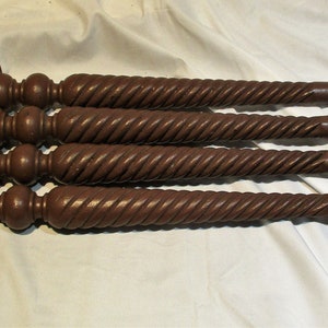 May include: Four dark brown wooden table legs with a twisted design and a rounded top.