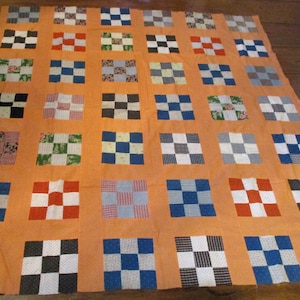 May include: A patchwork quilt with a variety of squares in different colors and patterns, including black, white, red, blue, and green. The quilt is made of a variety of fabrics, including cotton and linen. The quilt is laid out on a wooden floor.