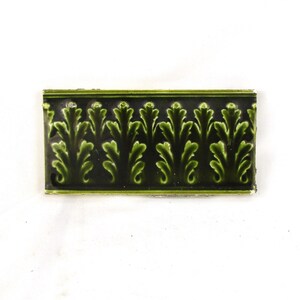 May include: A green and black ceramic tile with a repeating pattern of stylized leaves. The tile has a glossy finish.
