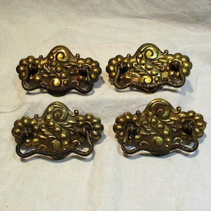 May include: Four antique brass drawer pulls with ornate floral designs and a rope-like handle. The pulls have a gold finish and are in excellent condition.
