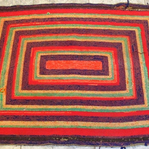 May include: A hand-woven rug with a multi-colored concentric square pattern. The rug is made of wool and has a rustic, vintage look.