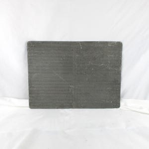 May include: A rectangular, dark gray stone slab with a textured surface. The stone has a slightly rough appearance and is set against a white background. The edges of the stone are rounded.