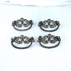 May include: Four antique bronze drawer pulls with ornate, filigree-style designs. Each pull features a curved handle and decorative detailing. The pulls are arranged on a white background.