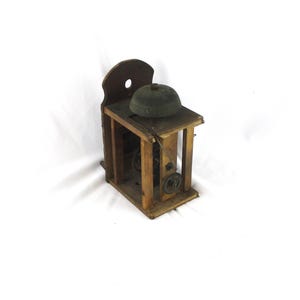 May include: An antique wooden bell with a dark green bell and a wooden frame. The bell is mounted on a wooden platform with visible gears and a wooden backboard. The overall design is rustic and vintage.