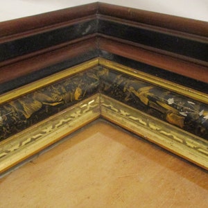 May include: Close-up of a corner of a picture frame with a black and gold design. The frame has a black and gold patterned border with a gold trim.