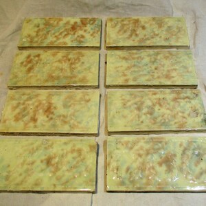 May include: Eight rectangular ceramic tiles with a yellow glaze and brown and green marbling. The tiles have a slightly textured surface.