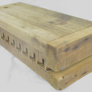 May include: A rectangular wooden mold featuring a natural light brown finish with visible wood grain. The object consists of two stacked blocks with a series of evenly spaced, notched cutouts along the side, joined by small metal nails.