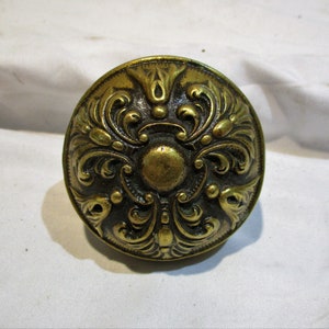 May include: A round, ornate brass door knob with a detailed floral design.