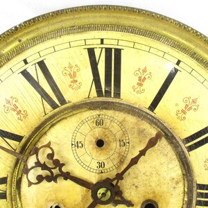 Peut inclure: Cadran d'horloge antique avec un cadre dor&eacute; et un cadran cr&egrave;me. Des chiffres romains noirs marquent les heures, avec des aiguilles noires indiquant l'heure. Des accents floraux rouges d&eacute;coratifs sont plac&eacute;s autour du cadran.