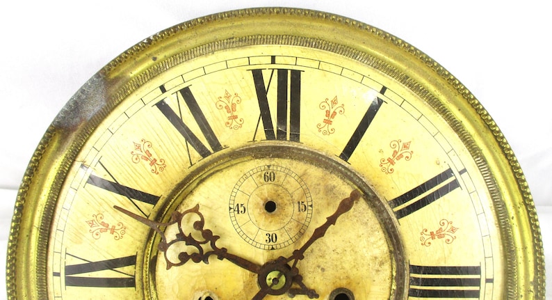 Peut inclure: Cadran d'horloge antique avec un cadre dor&eacute; et un cadran cr&egrave;me. Des chiffres romains noirs marquent les heures, avec des aiguilles noires indiquant l'heure. Des accents floraux rouges d&eacute;coratifs sont plac&eacute;s autour du cadran.