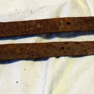 May include: Two rusty metal hinges, likely for a door or gate, with a simple design and a slightly curved shape.