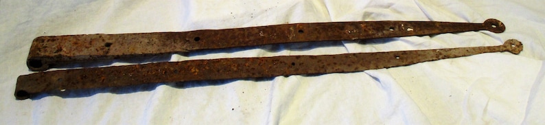 May include: Two rusty metal hinges, likely for a door or gate, with a simple design and a slightly curved shape.