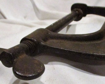 May include: A vintage cast iron C-clamp with a wing nut. The clamp is made of dark metal and has a smooth, worn surface.