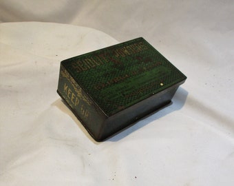 May include: Vintage rectangular tin box with a green and gold color scheme. The box features the text "SEDDON'S POWDERS" and "KEEP DRY" in gold lettering. The box has a textured pattern and appears to be aged.