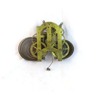 May include: A vintage clock movement with brass gears and a green-toned frame. The mechanism includes coiled springs and various gears, showcasing the intricate design of a mechanical clock. This antique piece is ideal for collectors or restoration projects.