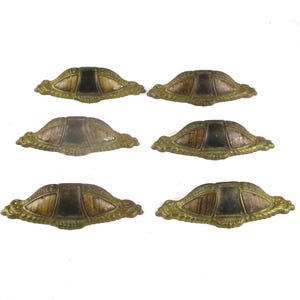May include: A set of six matching drawer pulls featuring an arched, metallic brass-toned finish with intricate embossed detailing along the edges. Each pull has a central dark, smooth rectangular inlay flanked by textured, wood-grain patterned panels.