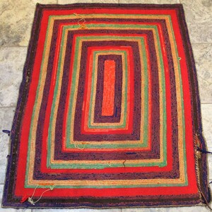 May include: A hand-woven rug with a multi-colored striped pattern. The rug has a rectangular shape and is made of natural fibers. The colors of the stripes are red, green, blue, and brown.